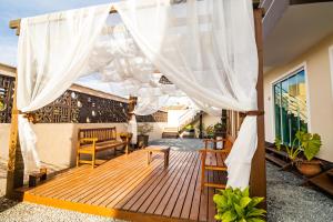 une terrasse couverte avec une terrasse en bois et des rideaux blancs dans l'établissement Hospedagem Morada Nativa Praia Bombas, à Bombinhas