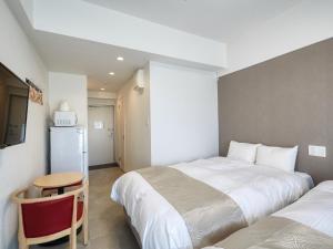 a bedroom with two beds and a table and a refrigerator at BiBi Hotel NAHA KUME in Naha