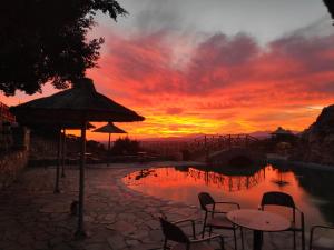a sunset over a pool with chairs and an umbrella at Arolithos Traditional Village Hotel in Tílisos