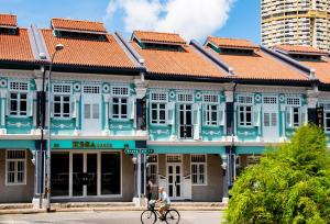 新加坡的住宿－KēSa House, The Unlimited Collection managed by The Ascott Limited，一位在蓝色建筑前骑着自行车的女人