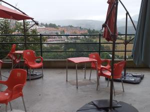 eine Terrasse mit roten Stühlen, einem Tisch und einem Sonnenschirm in der Unterkunft Albergue La Plaza in Tineo