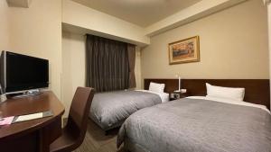 a hotel room with two beds and a desk and a television at Hotel Route-Inn Iyo-Saijo in Saijo