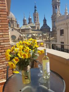 un jarrón de flores amarillas sobre una mesa con una botella de vino en El BALCÓN de PILAR, en Zaragoza