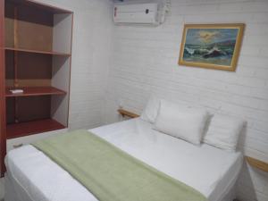a bedroom with a white bed and a painting on the wall at Apartamento estilo chalé - Enxaimel in Bombinhas
