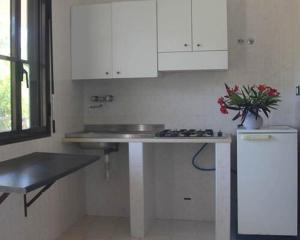 una cucina con armadi bianchi e un lavandino con fiori di Village Valle D'Oro ApartHotel a San Menaio