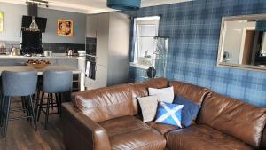 a living room with a brown leather couch and a kitchen at Holiday Apartment, Balloch, Loch Lomond in Balloch
