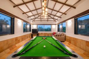 a pool table in a living room with windows at Classique Woods by StayVista with Lawn with Gazebo & Bar, Indoor Fun in Karjat
