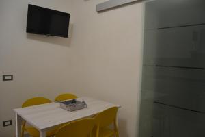 a white table with yellow chairs and a television on a wall at Il Birillo Casa Vacanze in Trapani