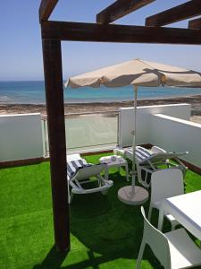 un patio con sombrilla y sillas y una pista de tenis. en On the Beach, en Corralejo