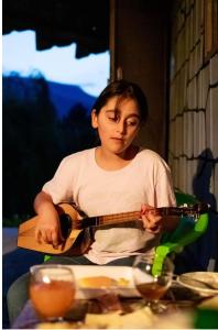 młoda dziewczyna grająca na gitarze przy stole w obiekcie Wooden house ,,Tsunda" w mieście Vardzia