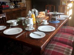 Balsporran Bed and Breakfast في دالوهيني: طاولة خشبية مليئة بالأطباق البيضاء والأكواب
