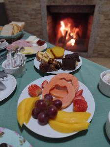 a table with plates of fruit and cakes and a fireplace at Pousada Encantos da Serra in Bom Jardim da Serra