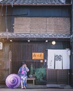 une femme assise devant un bâtiment avec un parapluie violet dans l'établissement Machiya Kikunoya Hanare, à Nagoya