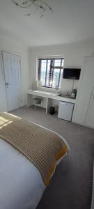 a white room with a bed and a desk and window at Barn Farm Guest House in Cold Norton