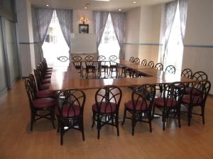 ein großer Tisch und Stühle in einem Zimmer mit Fenstern in der Unterkunft Hotel Sunrise21 in Higashihiroshima