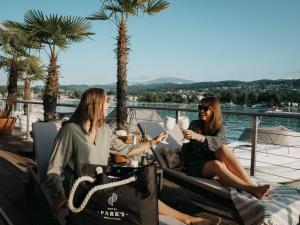 duas mulheres sentadas numa varanda com bebidas em Hotel Parks em Velden am Wörthersee