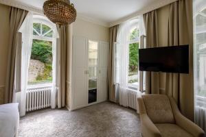a bedroom with windows and a chair and a tv at Villa Basileia Riverside in Karlovy Vary