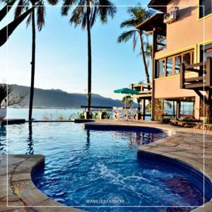 a swimming pool in front of a building with palm trees at Pousada Fruto do Mar in Ilhabela