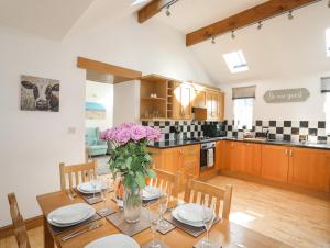 a kitchen and dining room with a table with pink flowers at Hazel Bank Cottage in Amlwch