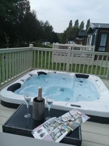 een hot tub op een terras met 2 glazen en een fles wijn bij JJs Lodge Azalea in York