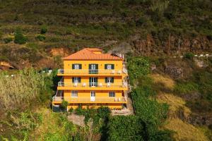 een geel huis met een oranje dak op een heuvel bij Sunset House in Arco da Calheta