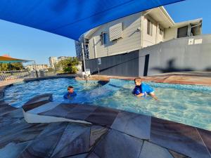 Dois rapazes estão a nadar numa piscina. em Alex Beach Cabins and Tourist Park em Alexandra Headland