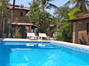 - une piscine avec 2 chaises et une maison dans l'établissement Golfinho Condomínio, à Arraial d'Ajuda