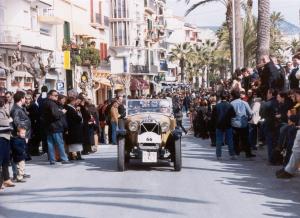 an old car driving down a street with a crowd of people at Hotel Piccadilly Sitges in Sitges