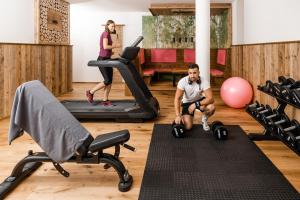 a man sitting on a fitness mat in a gym with exercise equipment at Embacher Sporthotel in Embach