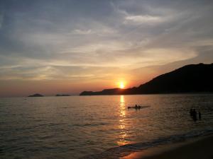 a sunset on the beach with two people in a boat at Chalé Vagalume Boiçucanga in Boicucanga