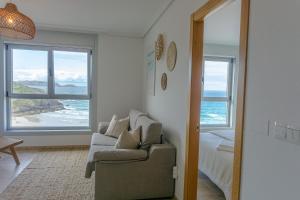 sala de estar con sofá, cama y ventanas en Apt ILUKA Nuevo con vistas al mar, en Malpica de Bergantiños