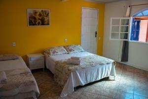 a bedroom with two beds and a yellow wall at Pousada da Bia in Rio das Ostras