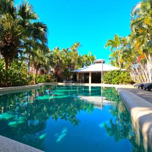 a swimming pool with palm trees and a house at Trinity Beach Club Holiday Apartments in Trinity Beach
