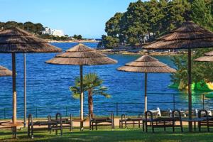 a group of tables and straw umbrellas next to the water at Ferienwohnung LUNA in Poreč