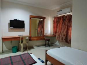 Schlafzimmer mit einem Bett, einem Schreibtisch und einem TV in der Unterkunft Hotel Geetha International in Thoothukudi