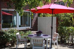 a patio table with a red umbrella and chairs at Ferienhaus Austernfischer in Butjadingen