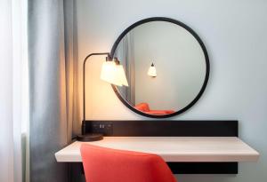 a mirror on a wall above a table with a red chair at Hyatt Place London City East in London
