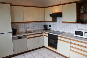 cocina con armarios blancos, fregadero y microondas en Ferienhaus Helten, en Lützkampen