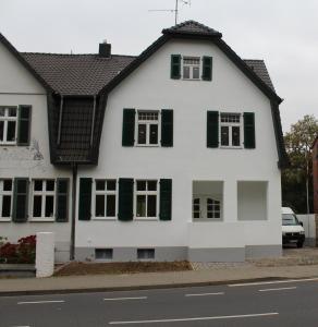 a white house with green shutters on a street at Haus Roy - Ferienwohnung Erdgeschoß in Zülpich