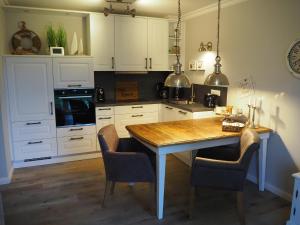 ツィングストにあるKajüteの白いキャビネット、木製テーブルと椅子付きのキッチンが備わります。
