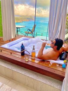 a man laying in a bath tub with a glass of wine at Pousada e Restaurante Vista Turquesa in Arraial do Cabo