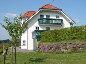 a white house with a balcony and a hedge at Ferienwohnung Leitges in Bettenfeld