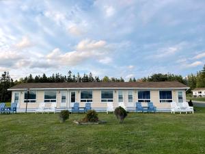 une maison blanche avec des chaises bleues dans la cour dans l'établissement Sea Breeze Motel, à Ingonish