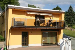 dos personas sentadas en el balcón de una casa amarilla en Ferienhaus Röbiger, en Klingenthal