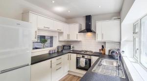 una cocina con armarios blancos y fregadero en Driftwood Cottage, Luxury character cottage in The English Riviera, close to the picturesque precinct of St Marychurch, a short walk to the stunning beaches of Babbacombe and Oddicombe! en Torquay