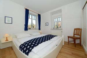 ein weißes Bett in einem Zimmer mit einem Stuhl und Fenstern in der Unterkunft Haus Amselnest Whg 04 in Wyk auf Föhr