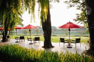 un patio con mesas, sillas y sombrillas en Cross Chiang Mai Riverside, en Chiang Mai