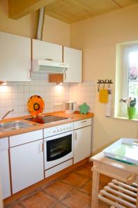 La cuisine est équipée de placards blancs, d'un évier et d'une cuisinière. dans l'établissement Ferienhof Rauert Haus 4, à Todendorf auf Fehmarn