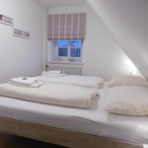 two beds in a white room with a window at FöhrZeit in Wrixum