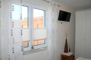Zimmer mit einem Fenster mit weißen Vorhängen und einem TV. in der Unterkunft Strandhafer V4W2 in Dierhagen
